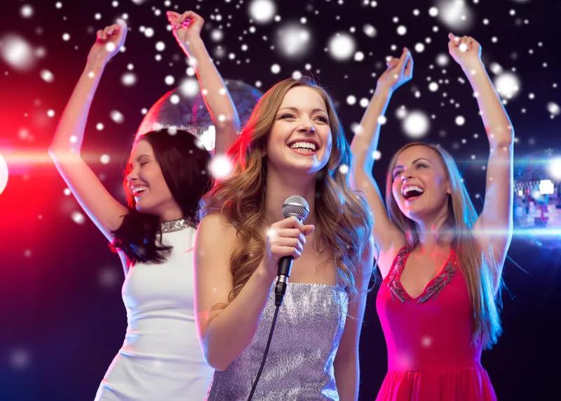 Drei Frauen singen und tanzen ausgelassen Karaoke auf einer Firmenfeier